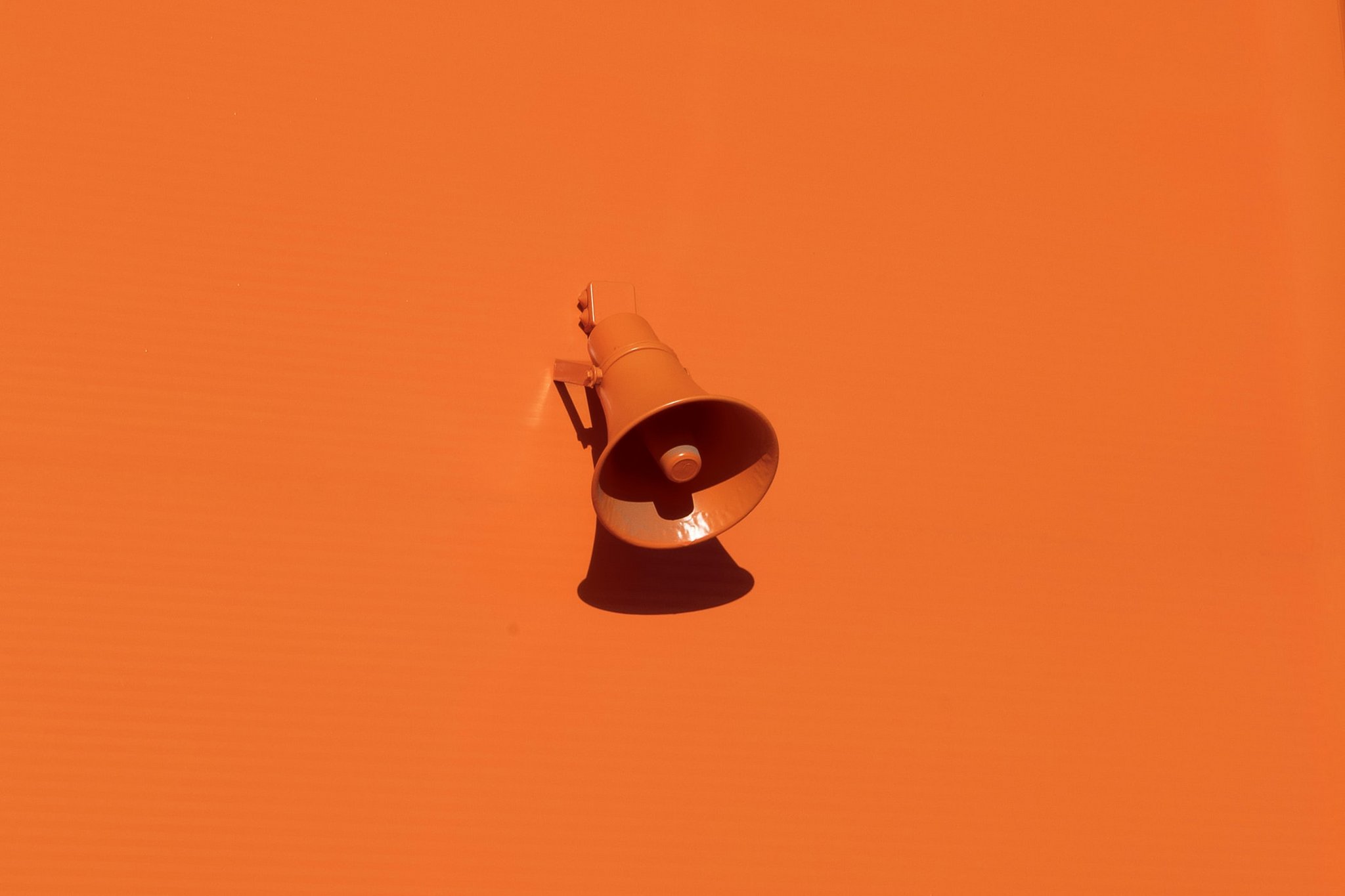 Das Bild zeigt eine orangene Wand mit einem Lautsprecher in der gleichen Farbe