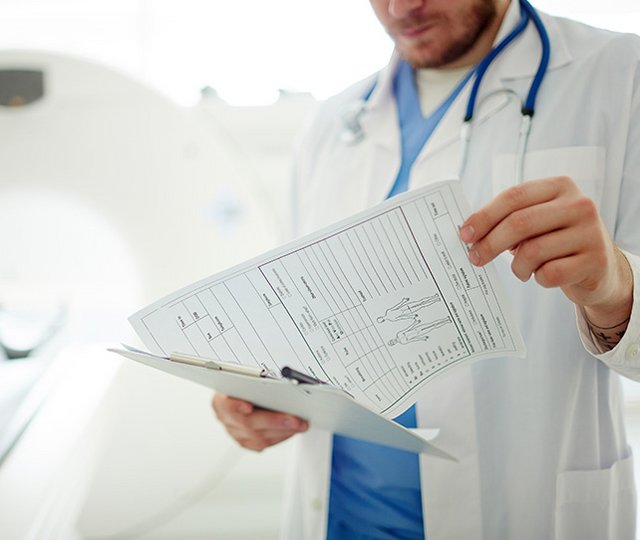 Das Bild zeigt einen Arzt vor einem Computer-Tomografen beim Lesen eines Patientenberichtes