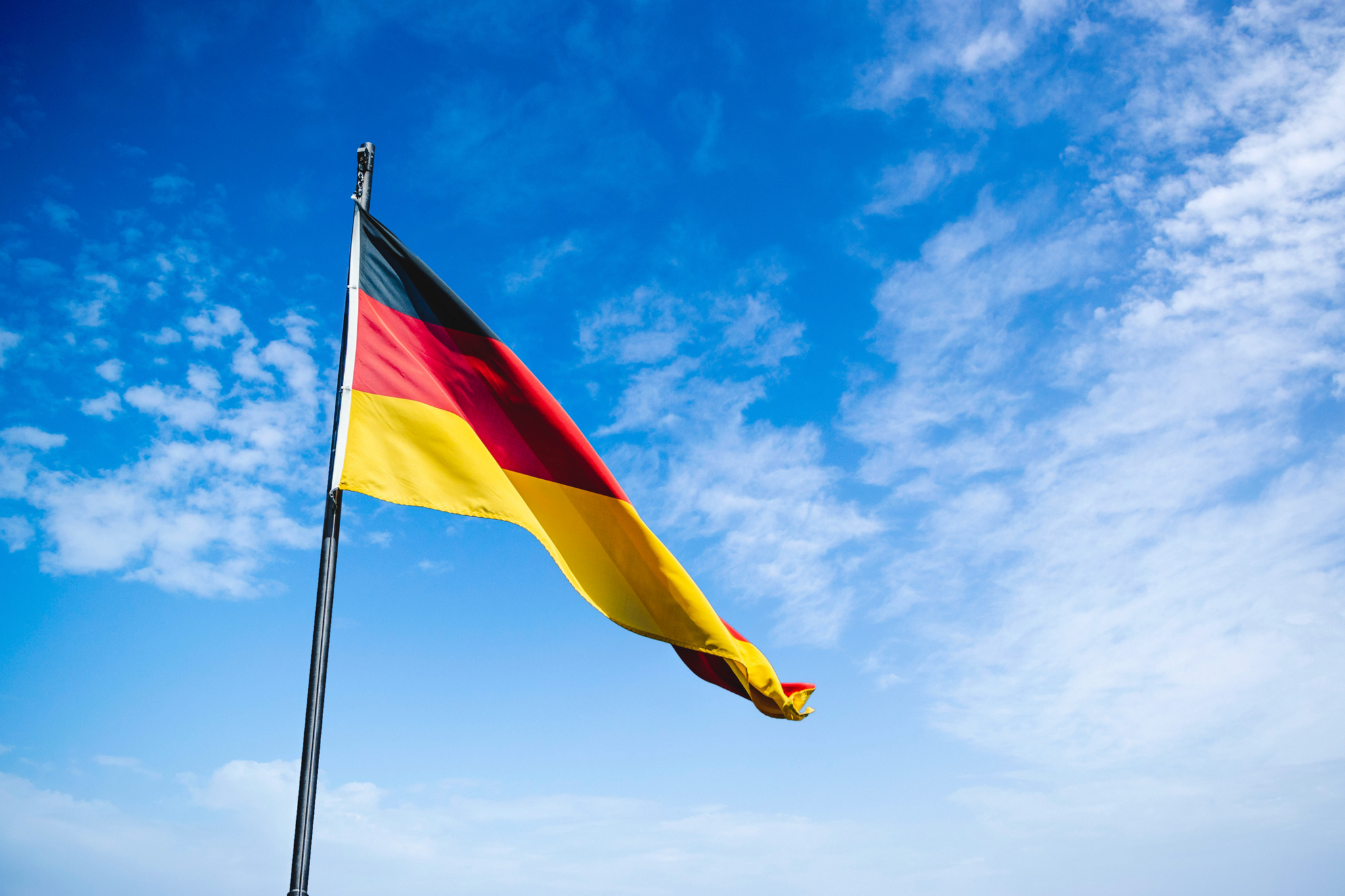 Das Bild zeigt die deutsche Flagge, die vor einem blauen Himmel weht