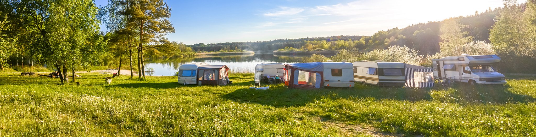 Das Bild zeigt eine Flusslandschaft mit Wohnwagen und Campern