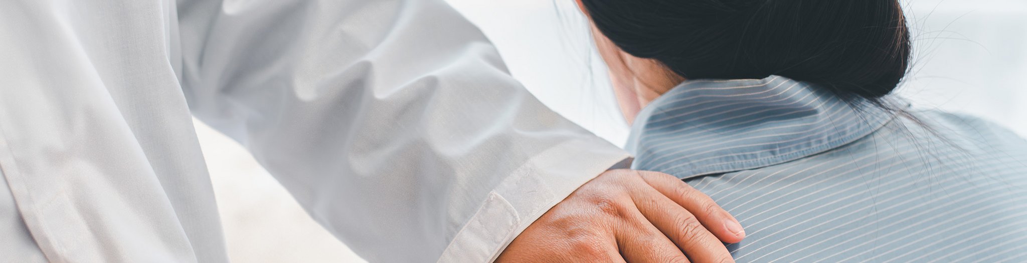 Das Bild zeigt die Hand eines Arztes, die beruhigend auf der Schulter einer Patientin liegt.