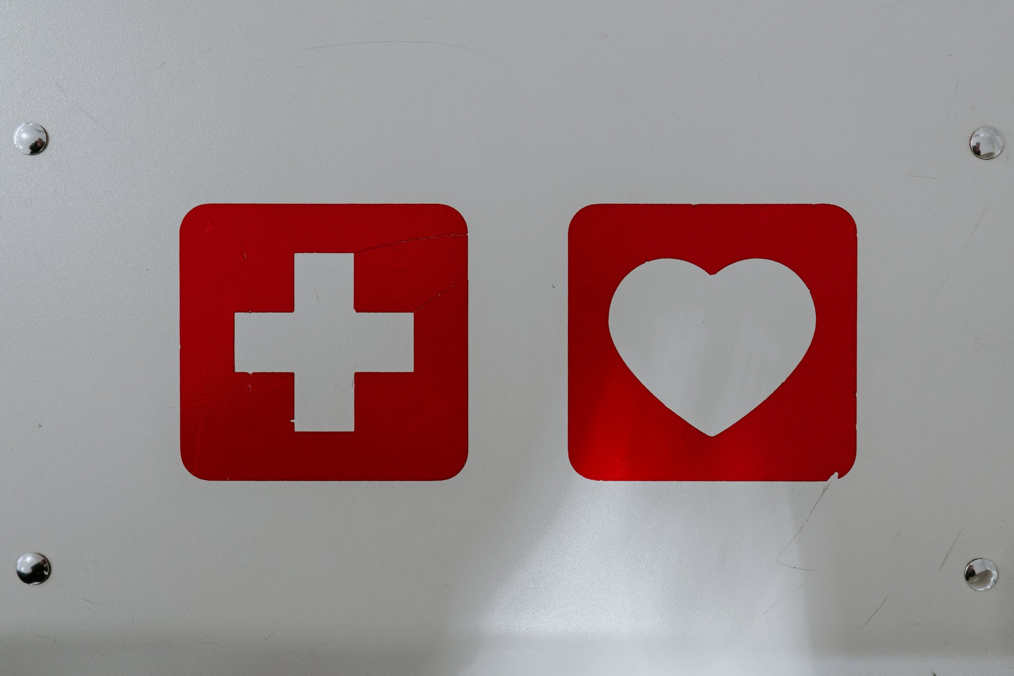 Das Bild zeigt Piktogramme eines roten Kreuzes und eines roten Herzens auf einer weißen Wand