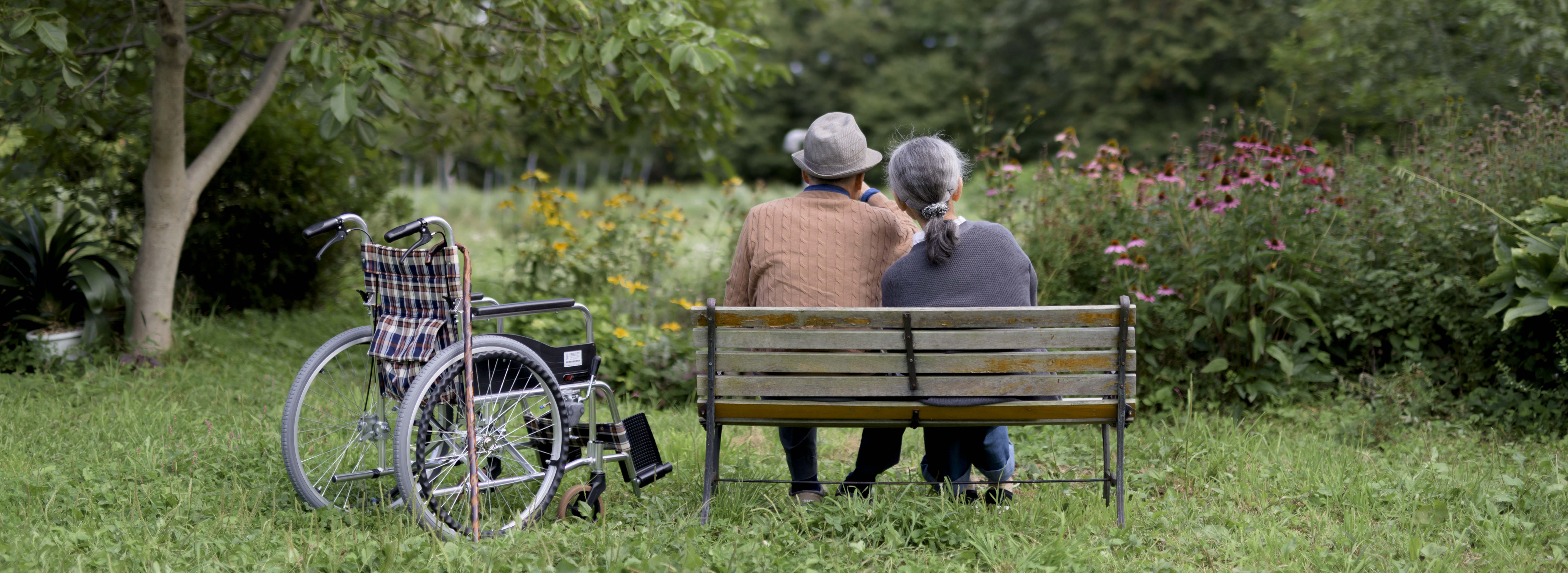 Älteres Paar auf einer Parkbank neben Rollstuhl