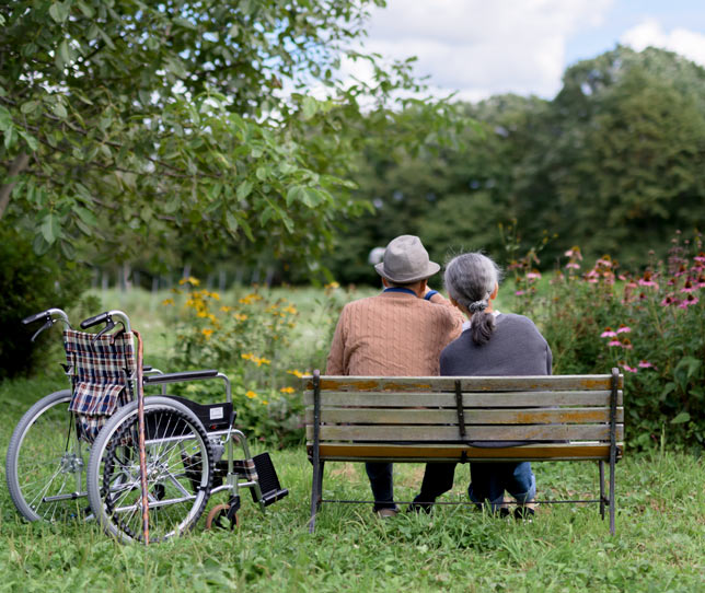 Älteres Paar auf einer Parkbank neben Rollstuhl