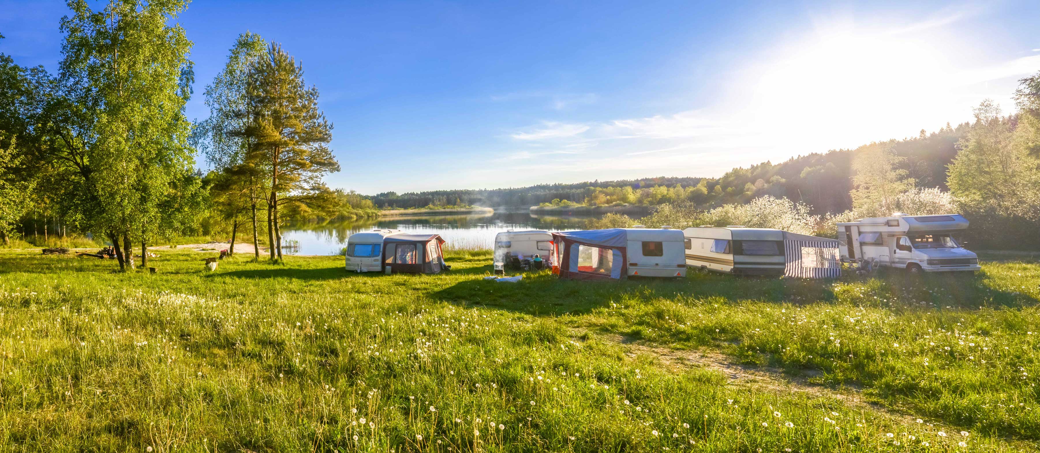 Das Bild zeigt einen Campingplatz an einem See, wo einige Wohnwagen parken