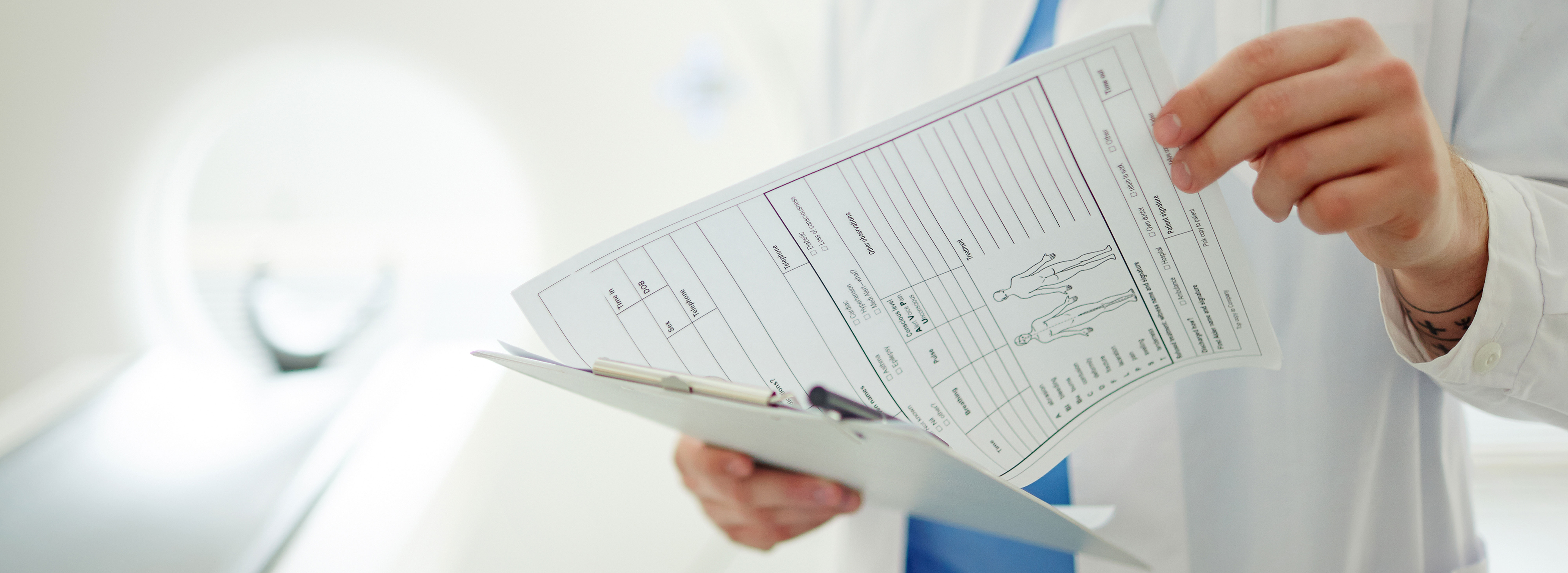 Das Bild zeigt einen Arzt vor einem Computer-Tomografen beim Lesen eines Patientenberichtes