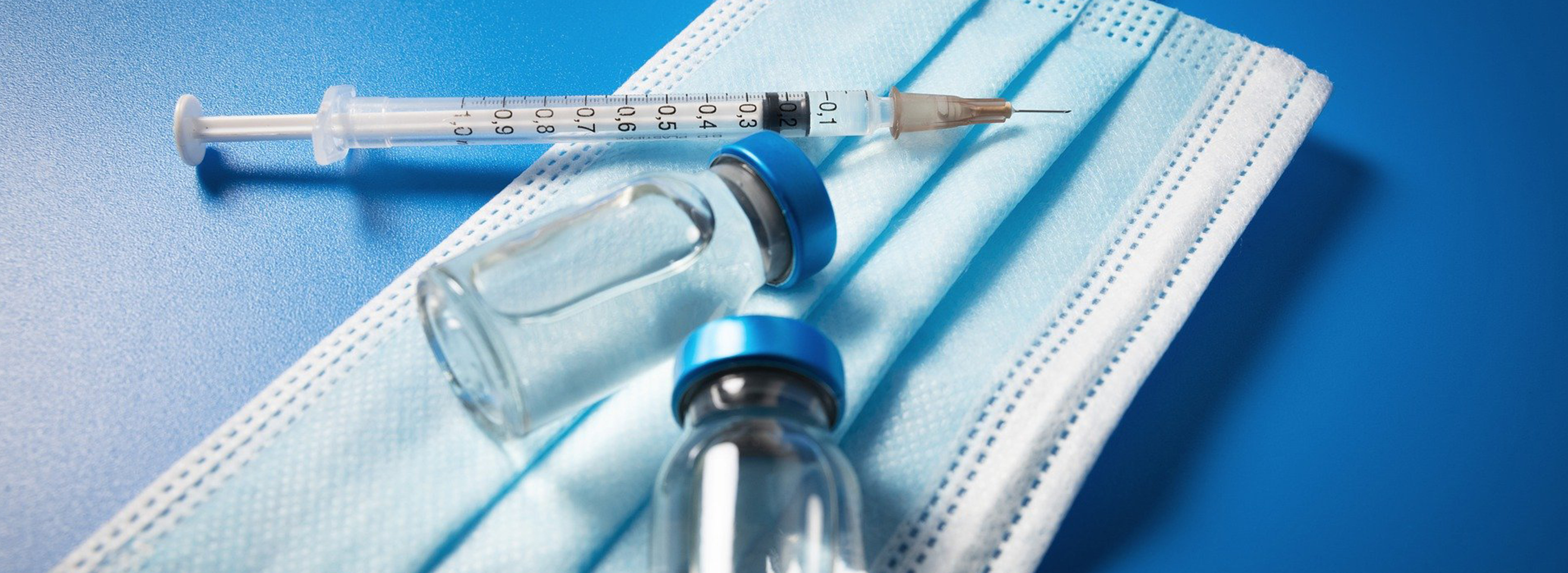 Das Bild zeigt eine Impfspritze, Impfmittel und einen Mundschutz