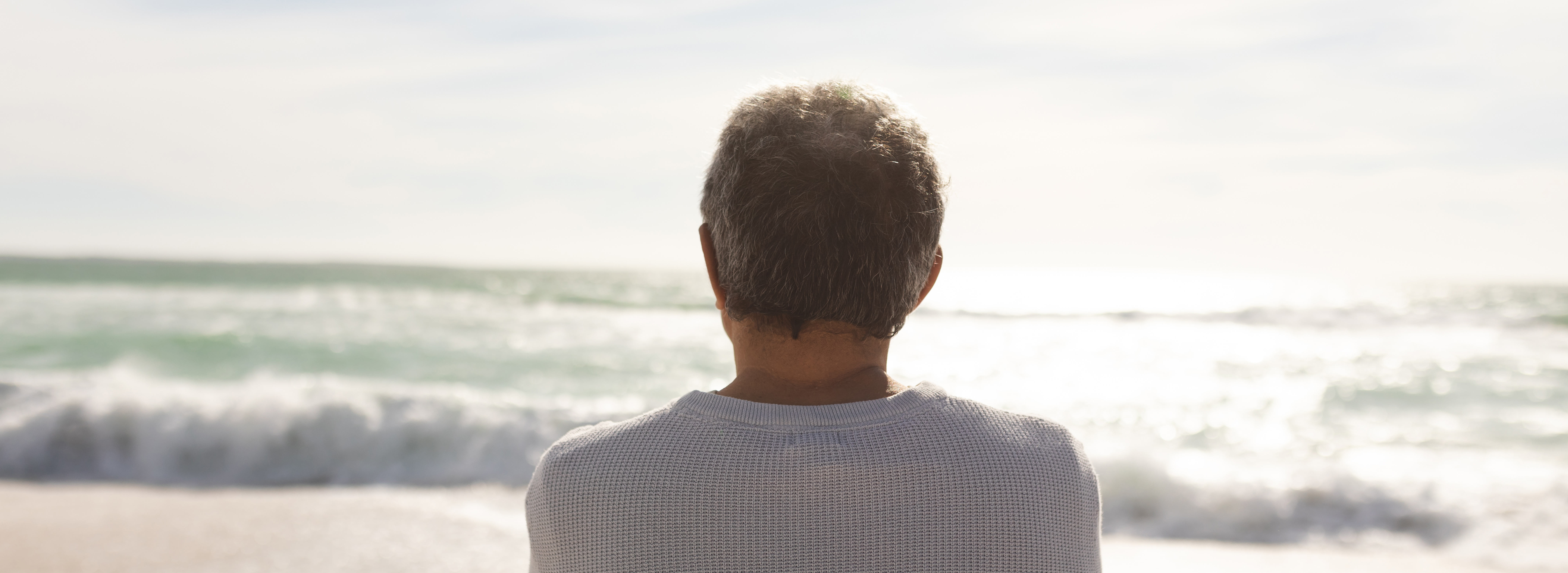 Das Bild zeigt eine Person von hinten mit Blick aufs Meer
