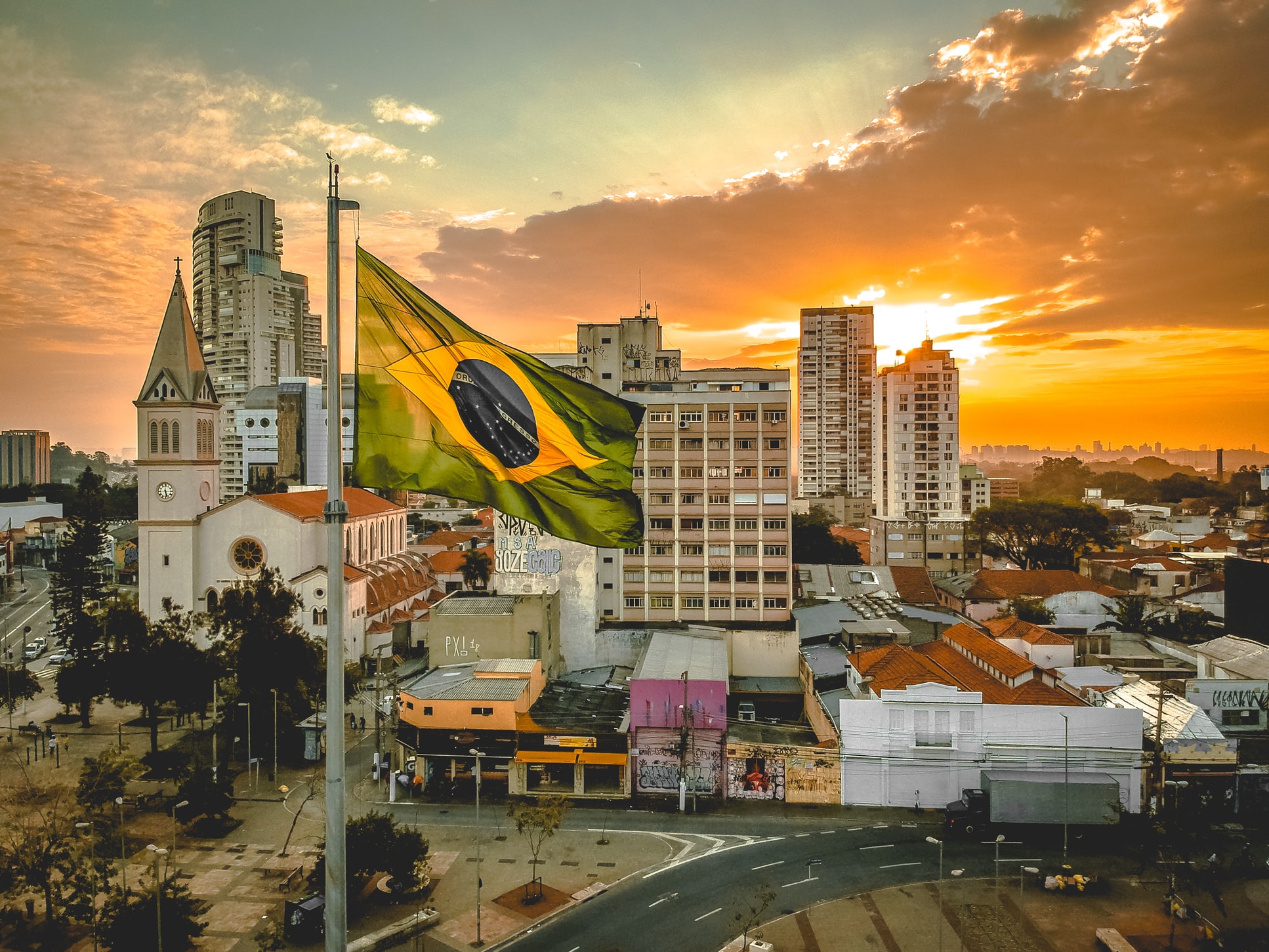 Das Bild zeigt Häuser einer Stadt, im Vordergrund weht die brasilianische Flagge