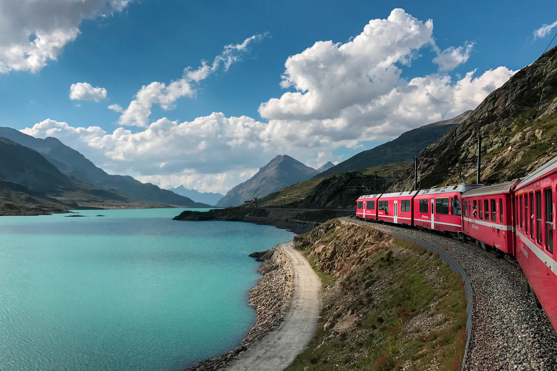 Das Bild zeigt eine Bahn, die in den Alpen einem See vorbeifährt